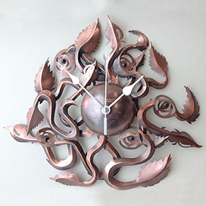 Climbing Roses Clock | Copper, clock mechanism and Garnets | Diameter 27 cm x Height 5 cm | Copper was scored by etching and oxidised. The garnets were bezel set in Sterling silver. Image of Climbing Roses Clock